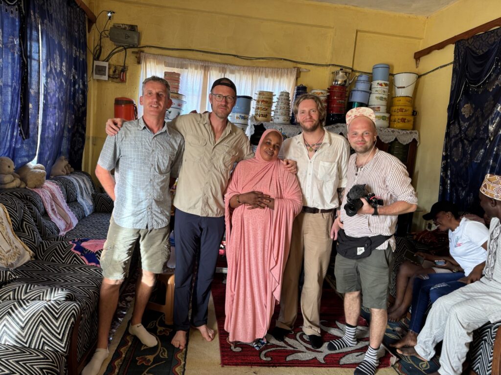 Pieci cilvēki stāv telpā un skatās kamerā