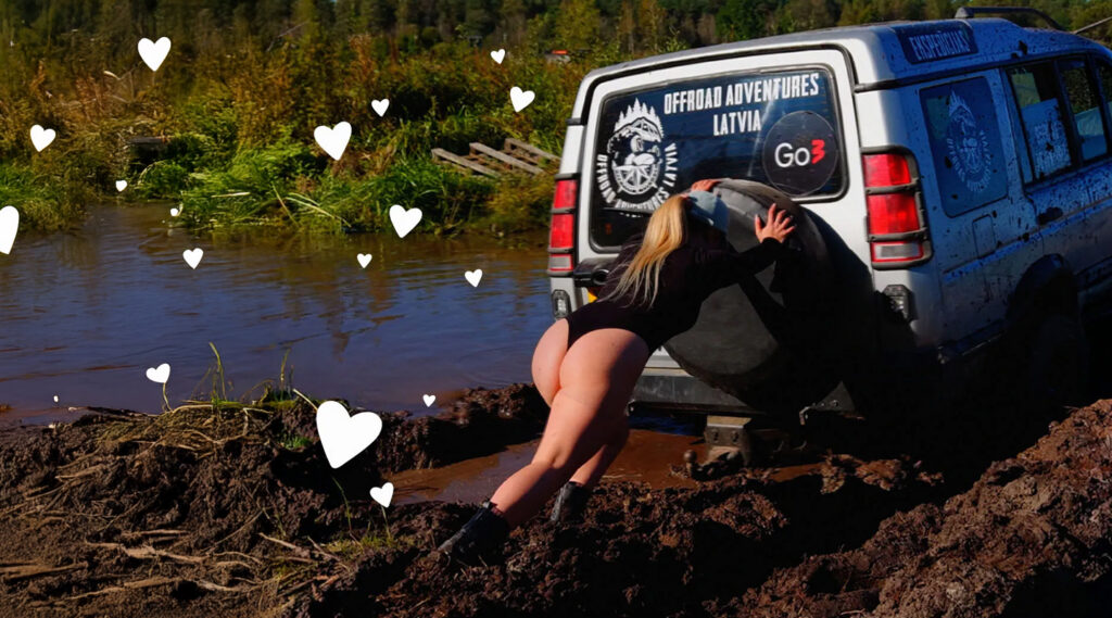 a woman is pushing a big car in the mud