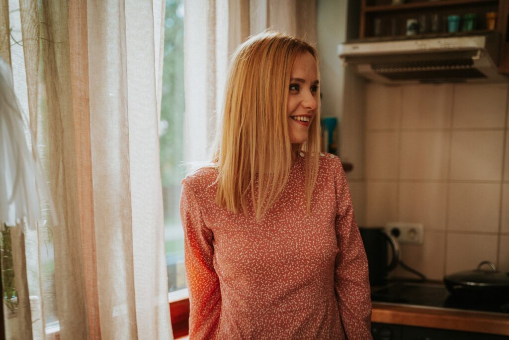 blonda sieviete ar sarkanu kreklu, kas skatās sānis virtuvē