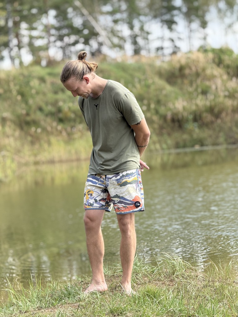 vīrietis, tērpies šortos, stāv pie ezera un skatās lejup