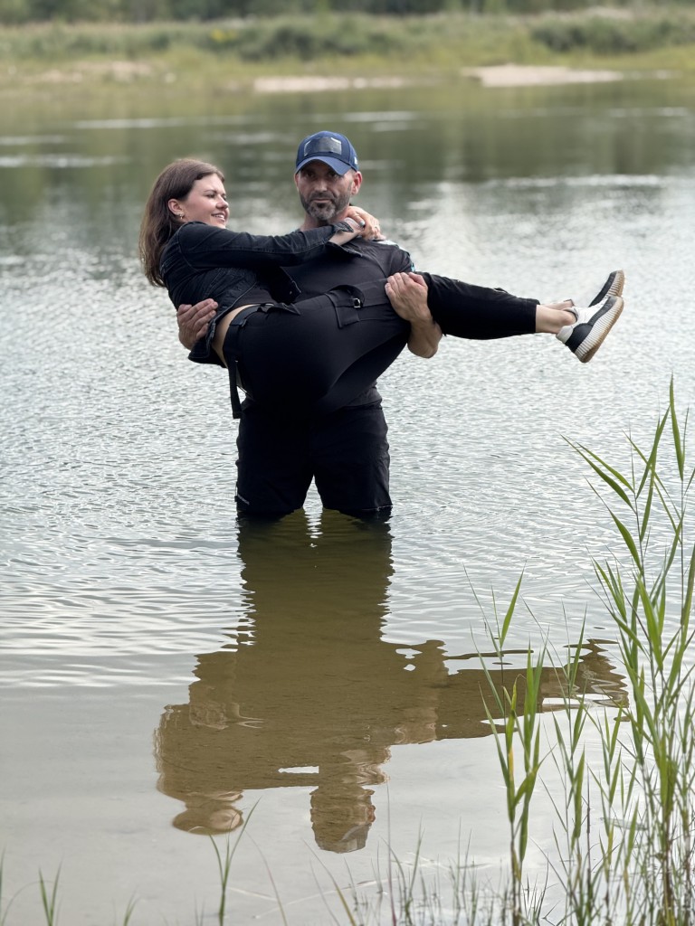 vīrietis tur sievieti savās rokās, abi atrodas ezerā
