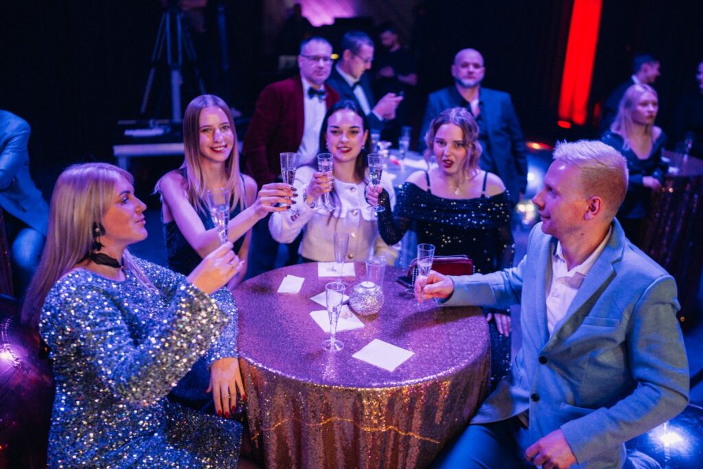 cilvēki ballītē paceļ glāzes
