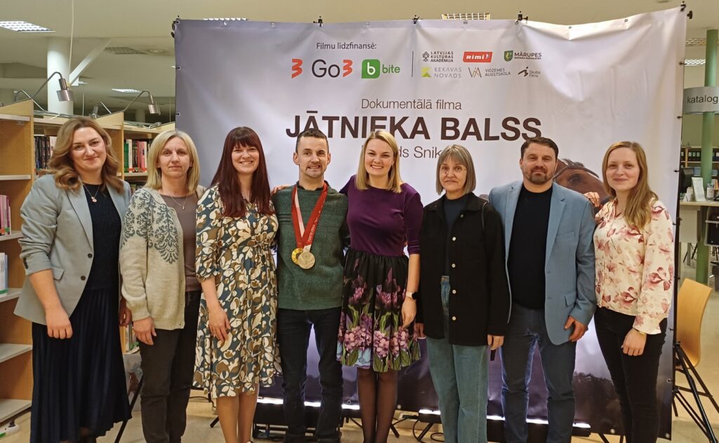 daudz cilvēku stāv pie bibliotēkas
