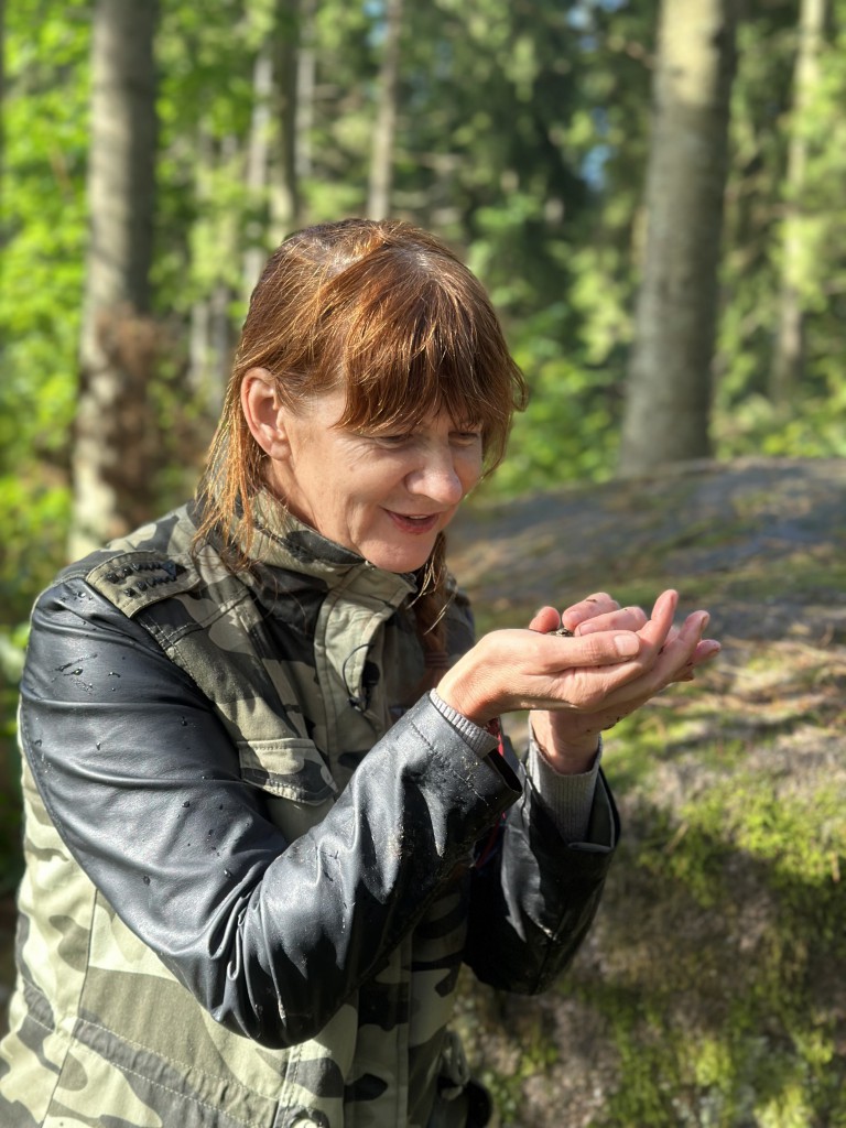 Sieviete zaļi melnā jakā skatās uz savām rokām.