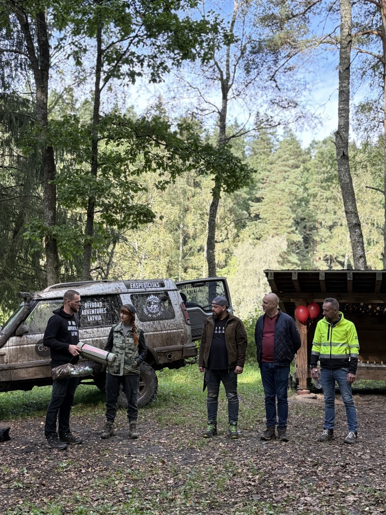 Viena sieviete un četri vīrieši stāv pie kravas automašīnas un mežā