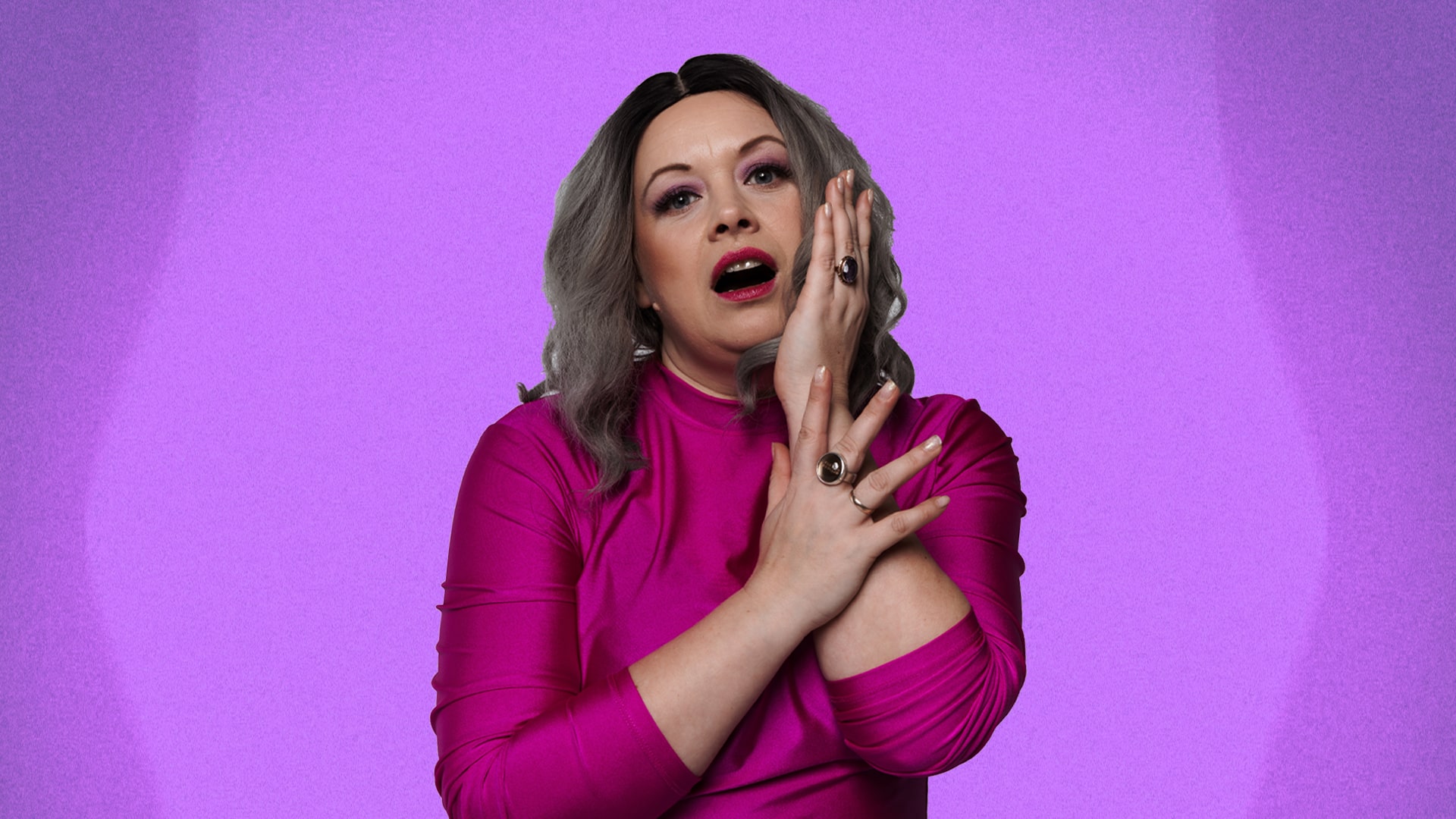 Blonda sieviete rozā apģērbā uz violetas fona, skatās tieši priekšā.