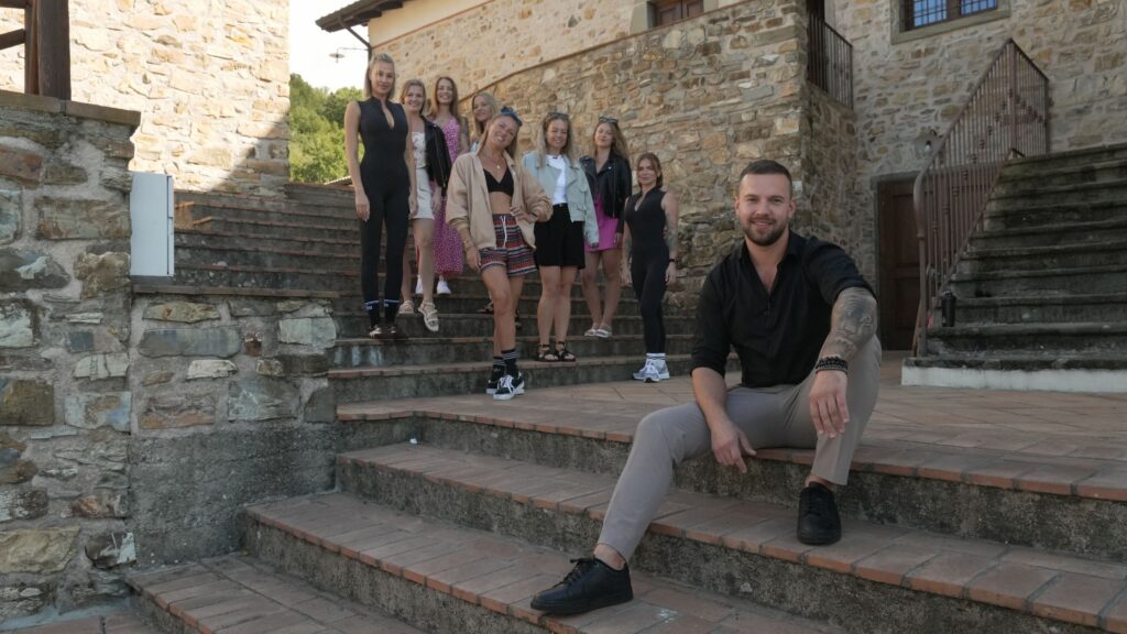 Vīrietis sēž uz akmens kāpnēm, un sievietes stāv viņam kreisajā pusē