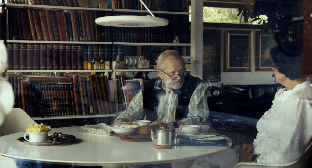 vecāka gadagājuma vīrietis sēž pie rakstāmgalda
